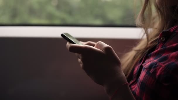 非常接近女人的手用手机。休闲格子衬衫。漂亮的女孩乘火车旅行。自然景观在窗口中的运动。侧面视图 — 图库视频影像