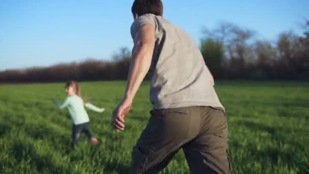 Gelukkige familie hebben een rust op een weide op een zonnige dag. Vader speelt catch-up met zijn dochtertje. Brede groene veld. Jonge Kaukasische familie. Chasing beeldmateriaal — Stockvideo