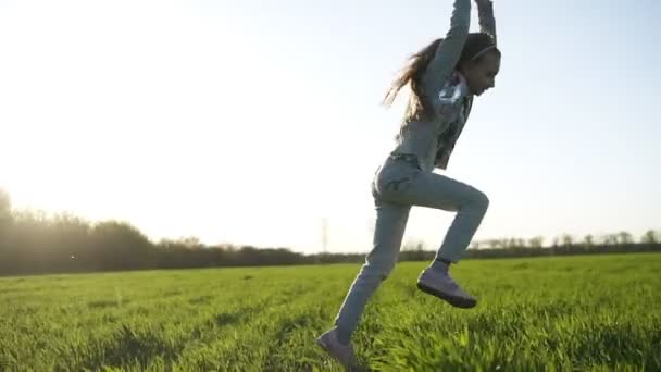 Petite fille aux cheveux longs en vêtements blancs joue à l'extérieur. Elle fait un saut périlleux. Une grande prairie verte. Fun et insouciant — Video