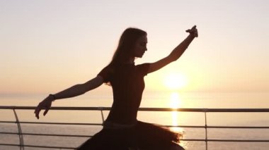 Dans eden balerin tutu ve okyanus veya gündoğumu veya günbatımı denize yakın pointe güzel sahne. Şehvetli genç kadın uzun saçlı klasik egzersizleri pratik. Ağır çekim