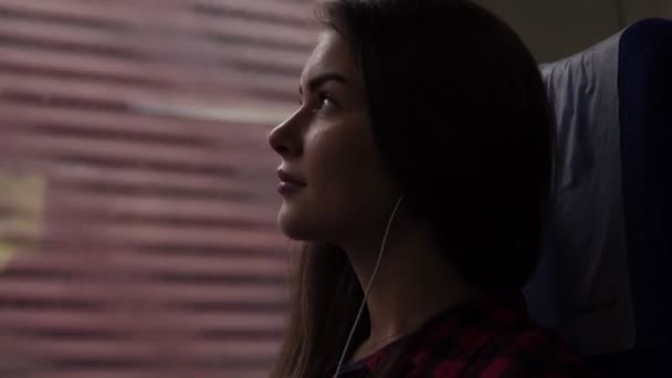 Pensive girl travels by train. Sitting next to the window. Looking up. Listen music in earphones. Thoughtful look. Side view — Stock Video