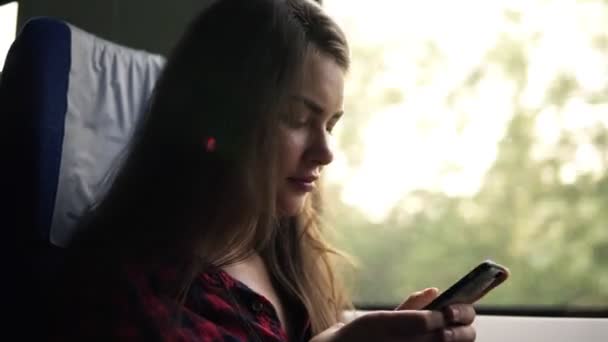 Zijaanzicht van de lage hoek van een mooi meisje in haar mobiele telefoon te typen. Gaan met de trein. Reizen. Natuur landschap in venster. Beweging — Stockvideo