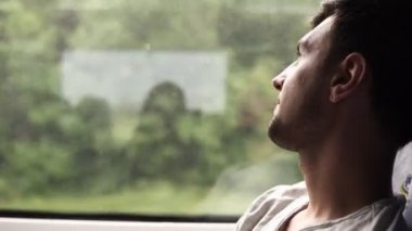 Profil düşünceli penceresine bakarak yakışıklı koyu saçlı adam. Trenle seyahat etmek. Kameraya bakıyor. Yolculuk hakkında heyecanlı. Gülümseyerek. Yan görünüm