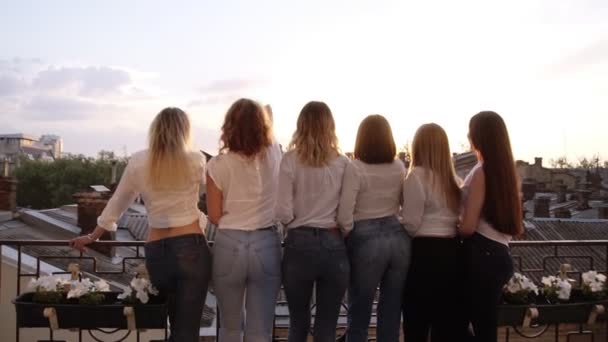 Filles caucasiennes avec de belles figures, dans les mêmes vêtements décontractés debout avec le dos à la caméra, s'appuient sur les balustrades du balcon. jeter des fleurs dans les airs. Enchanté. Dos . — Video