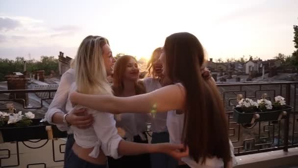 Raparigas felizes, abraçadas em círculo, vista lateral. Seis meninas atraentes abraçando, olhando um para o outro, de pé ao ar livre em um terraço. Rindo. Vista da cidade em segundo plano — Vídeo de Stock