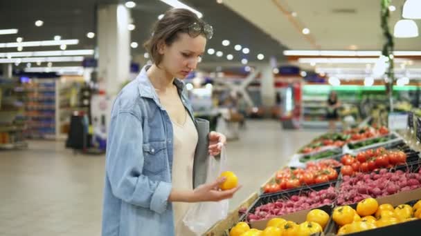 Compras. Mulher escolhendo bio alimento tomate amarelo na loja de vegetais ou supermercado. Toma um por um e coloca-o num saco de celofane. Tomates frescos amarelos — Vídeo de Stock