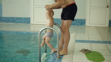 Havuzda yüzmek için oğulları öğretim anne. Genç aile havuzda yüzmek için oğlunu öğretim. Babası dışında havuzu, su, içine koyar çocuk anne yüzmek için ona yardım. Kapalı. Ağır çekim