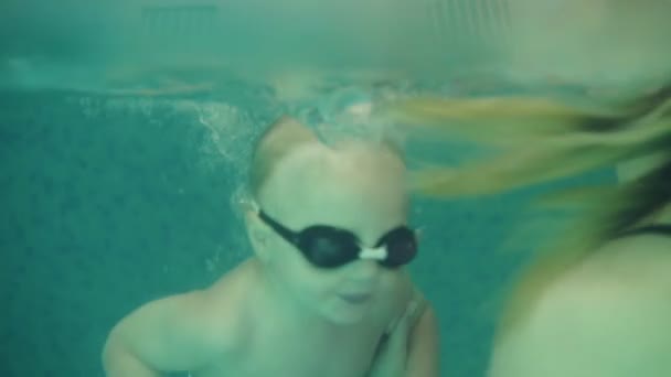 Close up de uma jovem beatutiful brincando e mergulhando com seu filho em uma piscina fechada. Criança feliz aproveitando o tempo. A mãe está a ensiná-lo a nadar — Vídeo de Stock