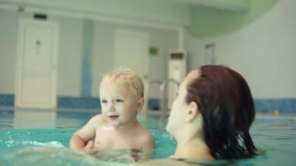 Genç bir ıslak kadın küçük sarışın oğlu ile yüzme kapatın. Su sıçramasına, döne döne. Mutlu bir zaman geçiriyoruz. Ebeveynlik. Kapalı Yüzme Havuzu — Stok video