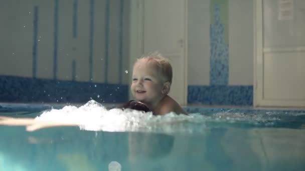 Junger Mann taucht unter Wasser. Rudern im geschlossenen Schwimmbad. Der kleine Junge liegt auf dem Rücken seines Vaters. Schmunzeln. Mutter umarmt sie. glückliche Familienzeit — Stockvideo
