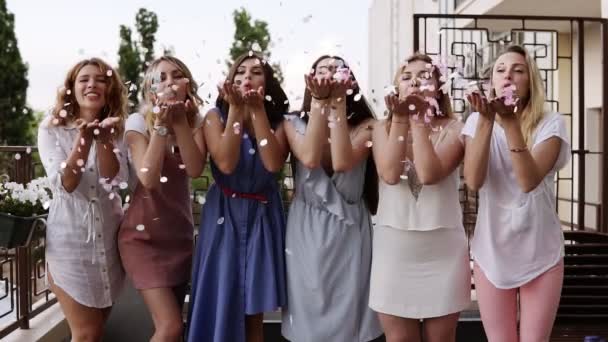 Front view of six attractive caucasian young women playfully blowing bright colored confetti from their hands together. stylish clothes. Bachelorette party. slow motion — Stock Video