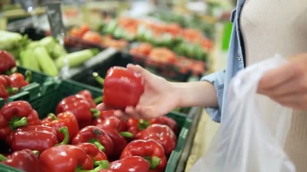 Kapesní záběry z dívčí ruce výběr čerstvé červené papriky z pole v oddělení zeleniny. Obchod s potravinami. Dívka dá paprikou na celofán taška — Stock video