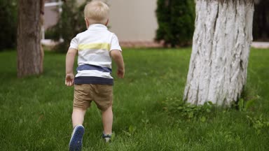 Baba ve oğul saklambaç oynayalım ağacın etrafında. Küçük sarışın çocuk çalışıyor. Mutlu saat. Ebeveynlik. Yeşil çimen çevresinde