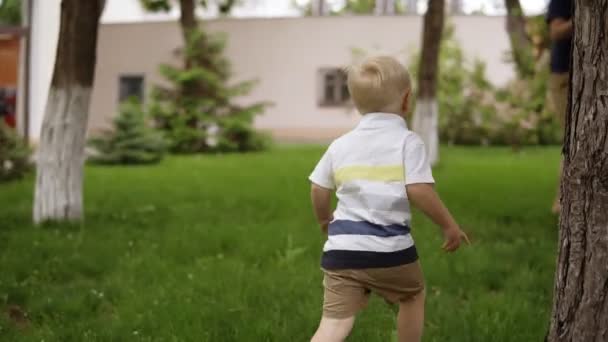 Un petit garçon joue avec son père caché et cherche dans le jardin. Il court joyeusement sur l'herbe. Le père attrape son fils, lève les mains et le retourne. Mouvement lent 