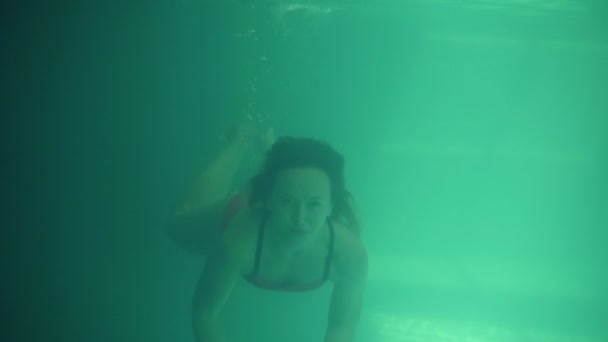 Mladá krásná žena, plavání v bazénu pod vodou. Nádherný pohled zepředu. Modré a zelené vody. Smilling