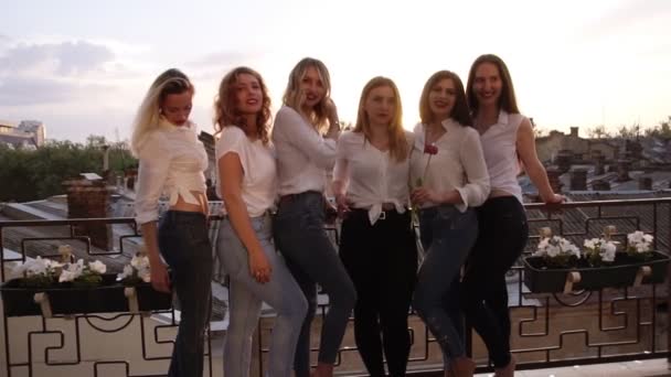 Seis chicas caucásicas están de pie en un balcón y posando para la cámara. Ropa casual. Primer plano de las niñas piernas en jeans. Fondo de la ciudad vieja — Vídeos de Stock