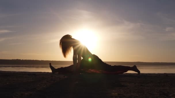 Jonge vrouw doen split, yoga houding buiten op het strand. Mooie silhouet van atleet. Zonsondergang — Stockvideo