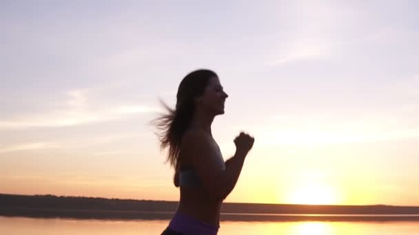 Imágenes de cerca de una chica en forma corriendo por el agua. Sunrise. La joven mujer entrena. Feliz, sonriente — Vídeos de Stock