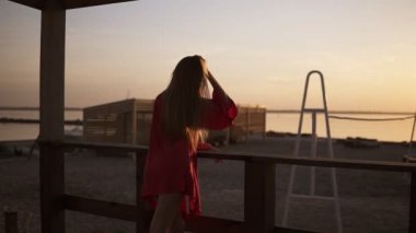Bir sabah deniz ya da okyanus gündoğumu güzel görüntüleri. Suya karşı karşıya kırmızı elbise ayakta çekici uzun saçlı sarışın kadın