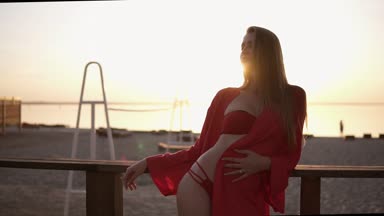 Kırmızı güzel mayo ayakta korkuluk plaj yakınında muhteşem beyaz modeli. Güneş parlıyor ve arka plandaki parlak su bulanık