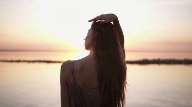Bir iskele üzerinde elbise duran güzel günbatımı ve gündoğumu sırasında poz güzel uzun saçlı bir kız Backview