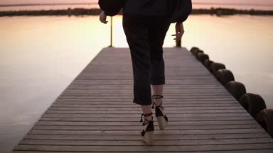 Uzun boylu, uzun saçlı bir kadın siyah giysilerle iskelede yürüyüş arka görüntüleri izleme. Elbise modeli. Güneş ışığı, sabah