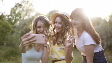 Piknik açık yapma üç güzel kız arkadaş grubu. Selfie fotoğraf smartphone üzerinden alırlar. Güneş parlıyor ve arka plan üzerinde
