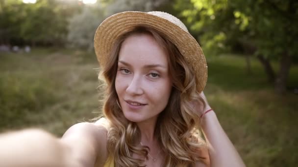 Молодая блондинка, делает селфи в соломенной шляпе, смешное лицо, позирует в сельской местности в летний день. На открытом воздухе — стоковое видео