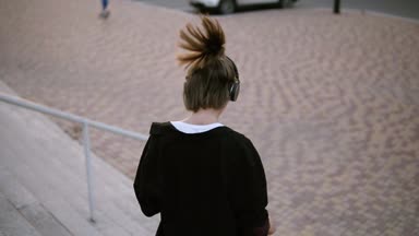 Şakacı parktaki merdivenlerden aşağı gidiş at kuyruğu ile mutlu şık kadın. Döne döne ve onun kulaklık müzik ile dans. Gülümseyerek. Duygu iyi