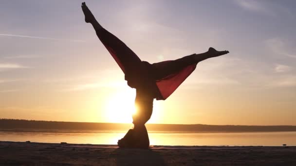 运动美丽的年轻高级瑜伽妇女站在倒立户外在海滩上。美丽的日落, 剪影 — 图库视频影像