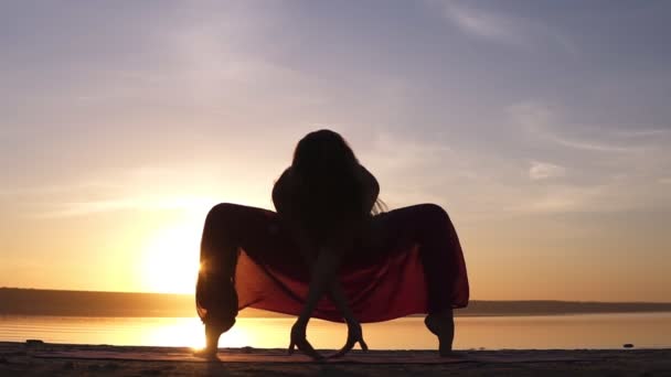剪影瑜伽妇女练习 Upaveshasana 在美丽的日落海滨。一个女人在瑜伽裤惊人的看法。前视图 — 图库视频影像
