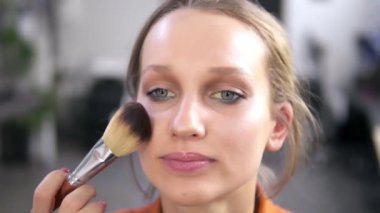 Güzel bir gülümseyen kadın model işlem makyaj sırasında önden görünümü. Sanatçı makyaj bir fırça kullanarak bazı toz koyarak iş tamamlar. Görüntüleri kapat