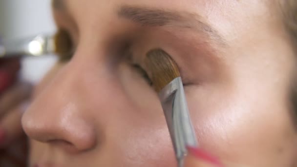 Make-up artiest toepassen licht bruin schaduwen op een oogleden met twee borstels samen, dicht omhoog van de ogen van een jonge Kaukasische dames — Stockvideo