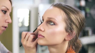 Makyaj stüdyosu. Profesyonel makyöz güzel bir beyaz modelin makyajını yapıyor. Fırça kullanarak göz farı sürüyorum. Göz makyajı.