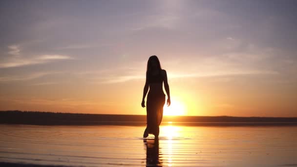 Fronte filmato di una splendida silhouette femminile passo su un acqua al mattino o alla sera crepuscolo. Ragazza snella in pantaloni yoga — Video Stock