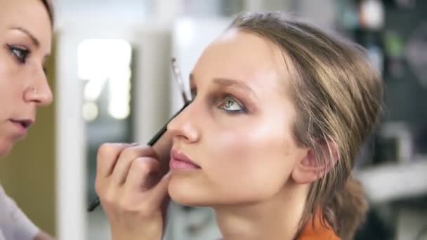 Make-up studio. Professionele make-up kunstenaar doet make-up voor een prachtig Kaukasisch model. Oogschaduw aanbrengen met een borstel. Ogen omhoog. — Stockvideo