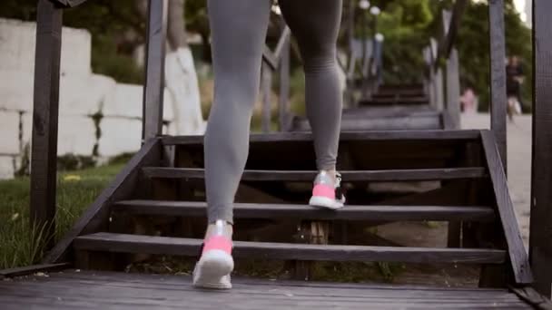 Вид спереду на дівчину, що займається на вулиці. Зсунувши ноги на сходах, стрибає. Красиві, треновані ноги в спортивному одязі, рожеві кросівки. Близько. На відкритому повітрі — стокове відео
