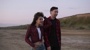 Güzel genç çift ekose gömlekler içinde açık havada akşam kumlu teritory üzerinde yürüyor. Birlikte dışarı asılı beyaz esmer çift, dostluk,