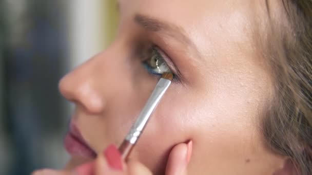 Zijaanzicht van een modellen gezicht. Make-up artiest eyeshadows onder het onderste ooglid met borstel toe te passen. Blauwe eyeliner. Proces — Stockvideo