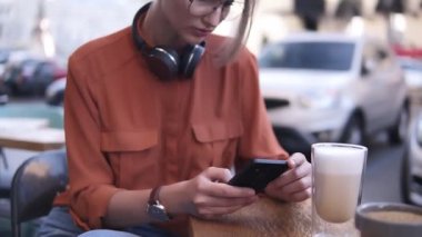 Saç bir bohça ve gözlük ile çekici bir sarışın kız bir bardak kahve içmek ahşap masa üstüne yanındaki sokakta bir kafede oturuyor. Kadın telefonda, konsantre yazarak