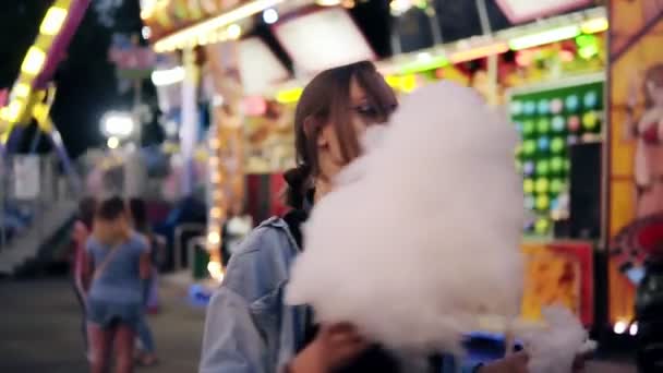 Una jovencita feliz está bailando, posando en la cámara. Una chica está pasando un buen rato en un parque de entretenimiento, ella está sosteniendo algodón dulce blanco — Vídeos de Stock