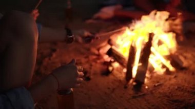 Genç hipster onun boyun kızartma hatmi şenlik ateşi sopa üzerinde kulaklık ile kadın, yakın çekim. Arkadaşlar ateşin yanında piknik kavramı oturuyor. Gece vakti