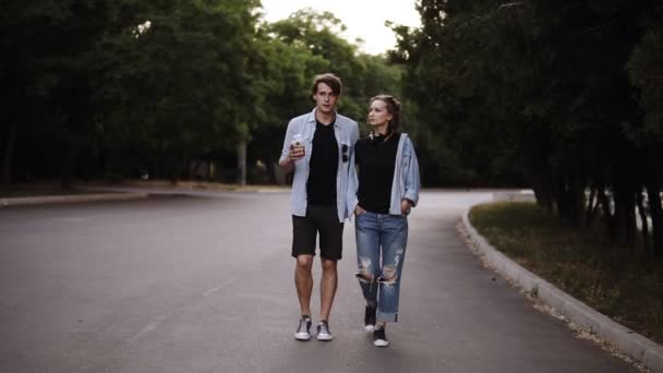 Stilvolle junge Leute spazieren durch einen grünen Park mit Bäumen und unterhalten sich. in lässiger, trendiger Kleidung. Frontansicht, Zeitlupe — Stockvideo