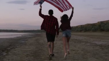 Genç kadın ve özgürlük hissi yükseltilmiş Amerikan bayrağı, kumla üzerinde çalışan adam. Akşam alacakaranlık. Görüntüleri izleme