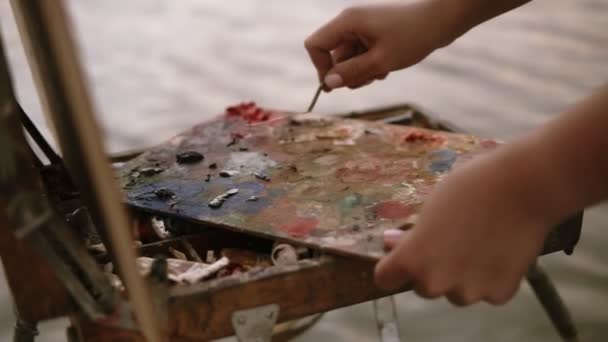 特写镜头的女性手, 谁混合油油漆或刮掉与调色板刀, 颜色的调色板上, 位于画架上。户外 — 图库视频影像