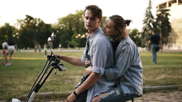 Pareja cariñosa pasando un momento relajante juntos sentados en minibicicleta en un abrazo cercano. Feliz sonrisa contenta, tierno beso. Lado del parque — Vídeo de stock