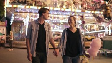 Güzel genç çift gülümseyerek, yürüyüş ve pamuk şeker, gece açık havada yemek elele lunapark, ziyaret etti. Erkek ve kadın gün faaliyetleri, rekreasyon yaşam tarzı zevk