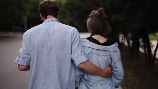 Filtrando imágenes de una pareja joven ambos en camisas azules similares están caminando unidos por el parque. Romance, calma, citas. Movimiento lento — Vídeos de Stock