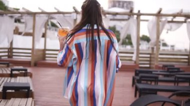 Araştırıyorum görüntüleri bir lüks moda kadın kokteyl yürüyen bir cam ile ipek sabahlık ahşap salon alanı deniz kenarında tarafından renkli. Yaz zamanı