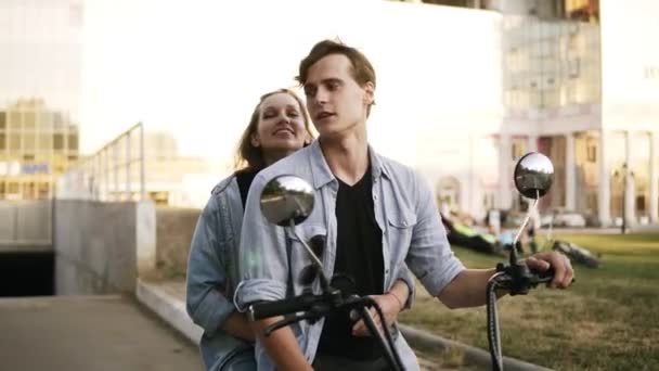 Junges attraktives Paar, das sich umarmt und amüsiert, während es auf einem Fahrrad auf der Straße sitzt. Beide trugen blaue Hemden. Sonnenlicht — Stockvideo